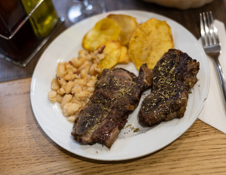 Grilled beef with spices and herbs with potatoes and beans on a white plate. Meat dish according to a traditional Spanish recipe