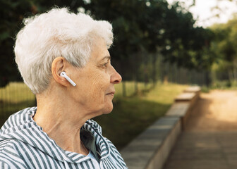Fototapeta premium An elderly woman with curly hair walks in a summer park and listening music.