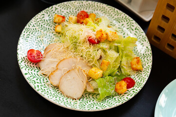 Just cooked Caesar salad served on white plate with green tracery.