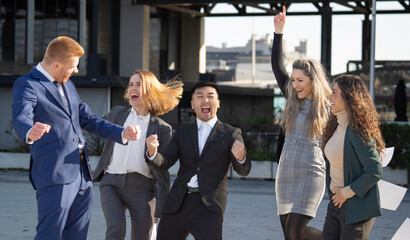 Euphoric multiethnic businesspeople cheering and expressing joy for achieving goals, celebrating victory and teamwork outdoors