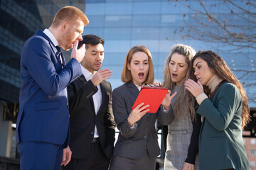 Obraz premium Shocked diverse businesspeople looking at digital tablet, reading unbelievable breaking news outdoors
