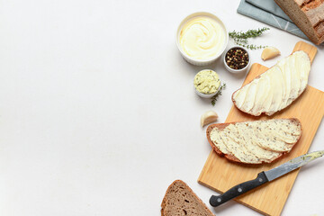 Wooden board of bread slices with fresh butter and different spices on white background