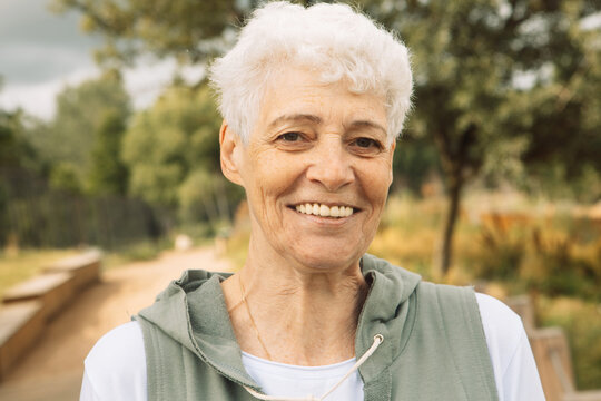 Portrait of smiling elderly woman at park. Happy thoughful mature woman relaxing outdoor.