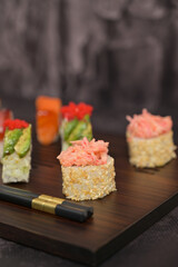Asian food. Assorted sushi roll with rice and fish on wooden serving board. Dark black texture background with copy space. Close up. Japan menu