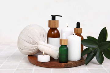 Set of spa supplies with different cosmetic products, herbal bag, towel and burning candles on beige tile table