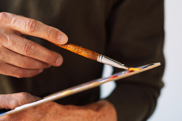 Close-up of male hands holding brushes and palette. Artist ready to create.
