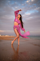 Graceful woman dancing on the beach at sunset in a flowing purple outfit