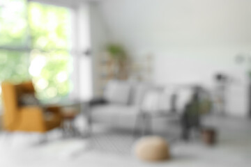 Blurred view of light living room with grey sofa, armchair and pouf