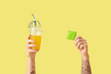 Male hands with condom and cocktail on yellow background