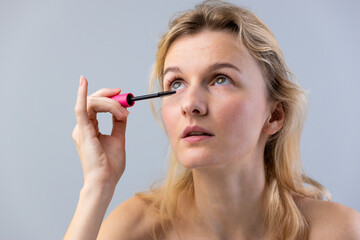Fototapeta premium A Young Woman Applying Mascara with a Pink Wand, Focused on Enhancing Her Eyelashes for a Beautiful Look and Capturing the Essence of Modern Makeup Techniques
