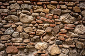 A close-up view of a textured stone wall with a mix of bricks and rocks, showing intricate patterns and aged materials