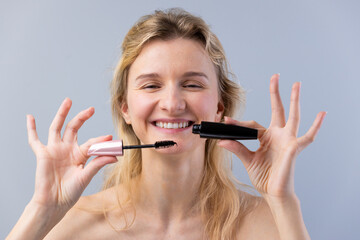 Young Woman Joyfully Holding Two Different Mascara Tubes in Front of Her Face, Signifying Makeup...