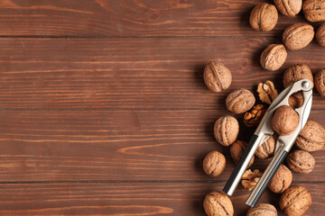 Many tasty walnuts and nutcracker on wooden background