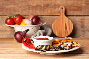 Plate with grilled vegetables and bowl with sauce on wooden table