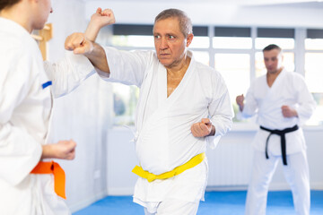 Obraz premium Elderly man and young man in kimono practicing karate techniques in gym