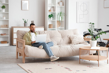 Freelance worker using laptop sitting on sofa in living room