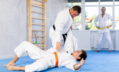 Concentrated karate sensei engaging kumite with young guy, working out fighting techniques in martial art training room..
