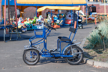 A blue pedal quad bike with a yellow canopy parked near an amusement park.