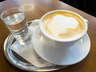 Creamy cappuccino with glass of water on wooden table in café setting