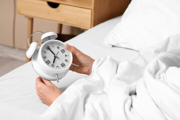 Female hands with white alarm clock in bedroom