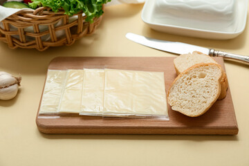 Board with slices of tasty processed cheese and bread on beige background. Closeup