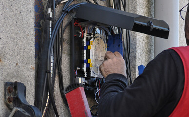 Person working on a ladder, making fiber optic connections in a box fixed to a street pole,...