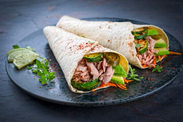 Italian style wrap piada wheat tortilla with tuna fish, vegetable and avocado served as closeup on a Nordic design plate