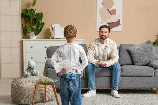Little boy hiding gift and greeting card for his dad behind back at home. Father's day