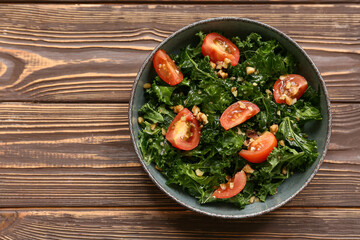 Bowl of tasty kale salad with tomatoes and walnuts on wooden background