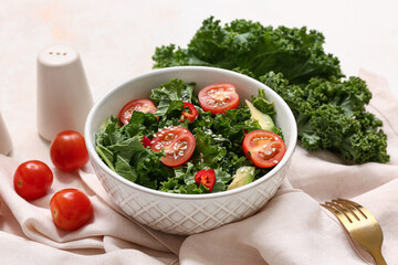 Bowl of tasty kale salad with tomatoes, avocado and napkin on light background