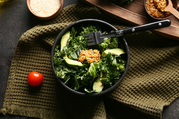 Bowl of tasty kale salad with avocado, Dijon mustard and napkin on dark background