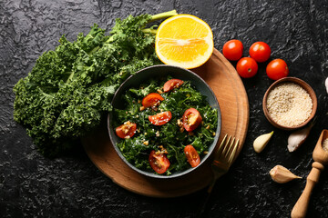 Composition with bowl of tasty kale salad and different ingredients on dark background