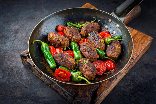 Traditional Croatian cevapi spicy meat ball rolls with tomatoes and paprika served as close-up in a rustic skillet