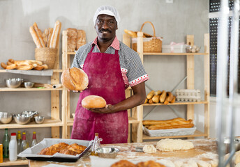 Male baker with basket of baked goods behind bakery counter inviting to buy fresh bread