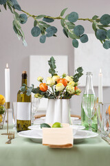 Festive table setting with citrus fruits, bottles of drinks, flowers and burning candles in room. Closeup