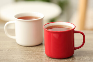 White and red mugs of hot tea on wooden table on blurred background. Closeup