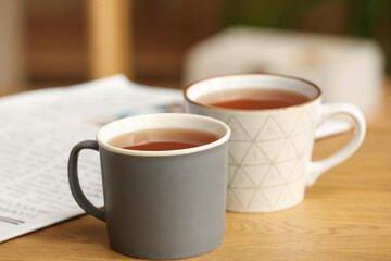 Mugs of black hot tea on wooden table on blurred background. Closeup