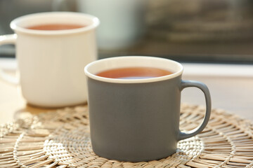 Cups of hot black tea on wicker mat against window. Closeup