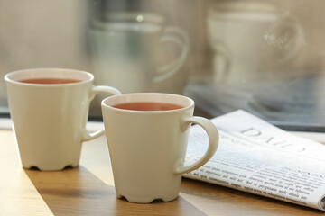 White cups of hot black tea on windowsill against window. Closeup