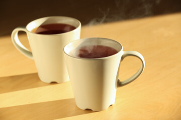 White cups of hot black tea on wooden table. Closeup