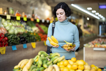 Female shopper carefully selects fresh bananas and other fruits in a grocery supermarket
