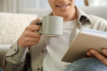 Young man drinking coffee and reading book at home. Closeup