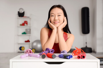 Sporty young Asian woman and skipping ropes on chest of drawers in gym