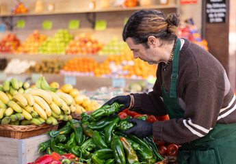 While working in shop, employee forms display case, puts ripe imported pepper in pile. Open display...