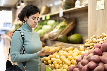Adult woman buyer choosing fresh potatoes in vegetable shop