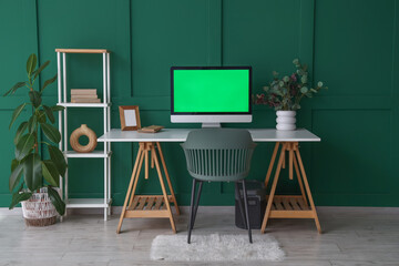 Modern workplace with computer and shelving unit near green wall in room