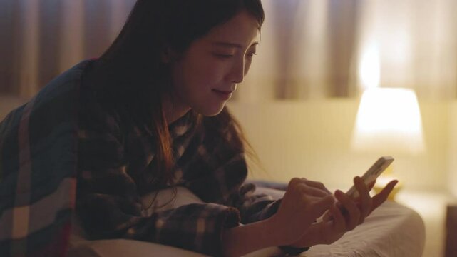 夜の寝室でスマートフォンを使用する日本人の女性