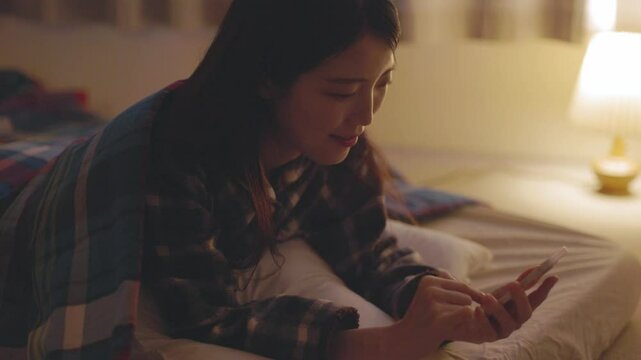 夜の寝室でスマートフォンを使用する日本人の女性