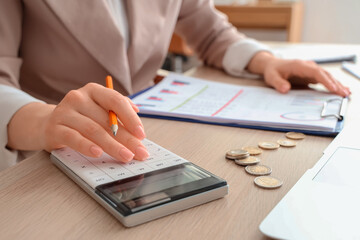 Woman with calculator, pen and coins at table in office