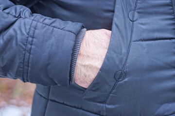 part of black winter jacket with hand in pocket on one man on winter street